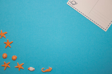 Turquoise background with postcard and seashells in the shape of starfish and seafood with empty space in the middle.