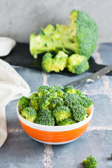 Pieces of raw broccoli in a bowl and a knife on the table. Close-up