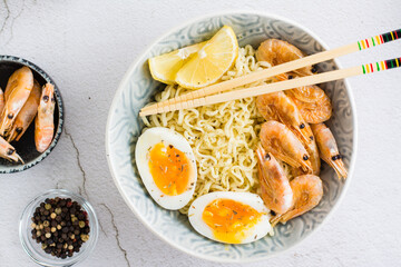 Chinese noodles with fried shrimp, boiled egg and lemon and chopsticks in a bowl. Top view