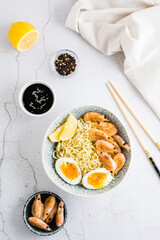 Chinese noodles with fried shrimp, boiled egg and lemon in a bowl. Top and vertical view