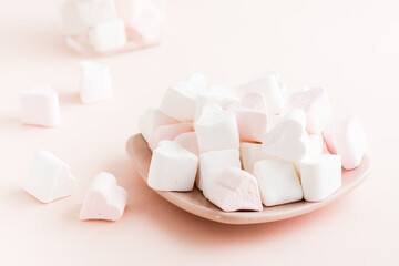 White and pink heart-shaped marshmallows on a saucer on a pink background