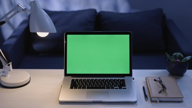 Modern laptop with mock up chroma key green screen on table of living room. Notebook with green screen for chroma key technology. Desk set up for work at home. Technology concept in 4k template