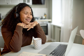 African girl in headphones looking at laptop screen watching movie or online webinar, enjoying...