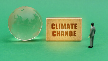 On the green surface is a globe and a figurine of a man who looks at a sign with the inscription - climate change