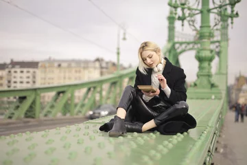 Plexiglas foto achterwand young woman sitting on a bridge in budapest with a book in her hand © olly