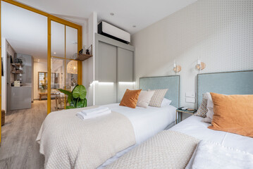 Bedroom with twin youth beds and glass and metal sliding wall at bedroom entrance, towels on bed, cream colored blanket and light blue fabric upholstered headboards