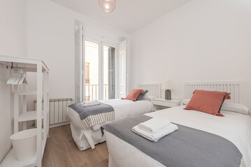 bedroom with twin beds with white wooden headboards, white bedding with tile-colored cushions, gray blankets, white wooden shelves and balcony with wooden shutters