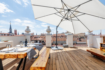 Terrace with large white fabric umbrella with wooden floors, solid wood dining table with benches...