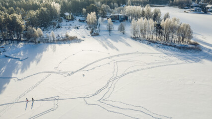 Top drone view of skiing people on snowy field near cottage village.