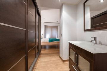 Walk-in closet with dark wood sliding door wardrobe with porcelain sink on matching wood cabinet with framed mirror