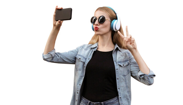 Portrait of young woman taking selfie by smartphone in wireless headphones listening to music isolated on white background