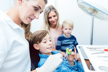 Family looking at boy choosing the colourful dental braces with female dentist doctor in clinic