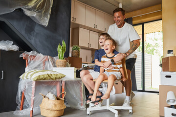 Full length portrait of happy family moving into new house with carefree father playing with...