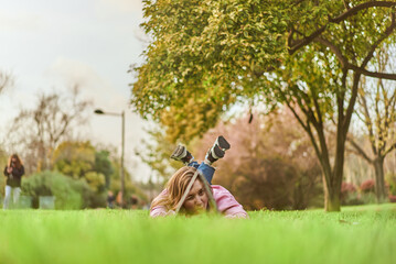 young woman smiling trough a laptop while laying in the grass of a park
