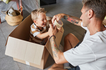 Portrait of happy father playing with cute boy in cardboard box while packing for family moving...