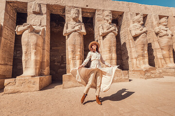 A happy tourist girl in a dress is interested in Egyptology and archaeology and gets a travel experience at the Karnak Temple in Luxor. - obrazy, fototapety, plakaty
