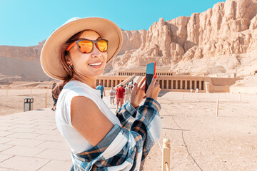 Travel blogger girl takes pictures on a smartphone at the famous Hatshepsut temple in the ancient...