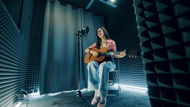 A lady is playing the guitar and singing in the recording studio