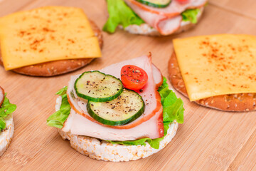 Light Breakfast. Quick and Healthy Sandwiches. Rice Cakes with Ham, Tomato, Fresh Cucumber, Green Salad and Cheese on Wooden Cutting Board. Beige Background