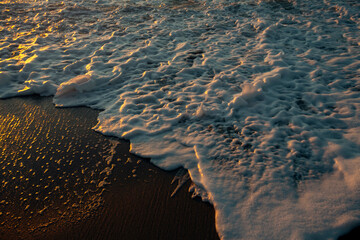 Reflection of the sun in the foamy surf during sunset on the ocean coast.