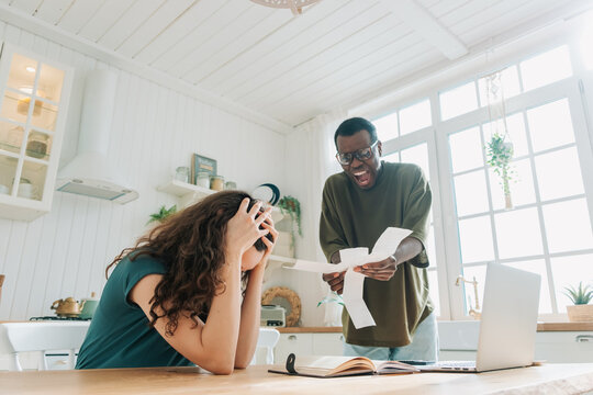 African American Man Scolds White Woman For Spending Too Much Money On Shopping Showing Checks. Multinational Couple Quarrels In Kitchen At Home