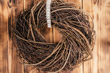 Tightly woven hanging willow wreath from wickers with tape lace in the center. Rural brown wooden and planking wall on background. Vintage country farmhouse seasonal Scandinavian decoration. Closeup