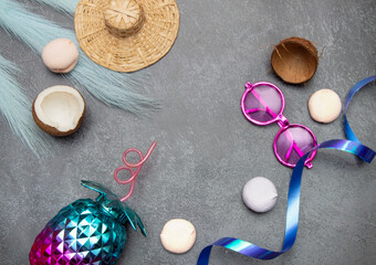 Summer tropical background in blue and pink tones with a pineapple glass, leaves, pink glasses, marshmallows, straw hat and coconut on a gray background under a stone. A postcard with a place for text