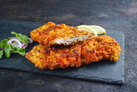 Traditionelles frittiertes Schnitzel mit Zitronenscheiben und Zwiebelringen serviert als close-up auf einem schwarzen Tablett mit Textfreiraum