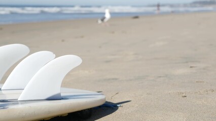 Surfboard for surfing lying on beach sand, California coast, USA. Ocean waves and white surf board...