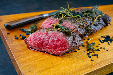 Traditional fried dry aged angus beef filet roast and medallions natural with herbs and black salt served as close-up wooden design board