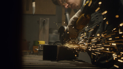 A man works with a circular saw. Worker grinder grinds metal in workshop. Sparks fly from hot...