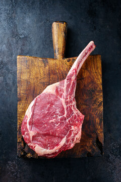 Raw dry aged chianina tomahawk steak offered as top view on an old rustic wooden board