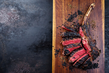 Modern style barbecue dry aged Chianina tomahawk steak sliced and served as top view on a wooden...