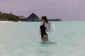 Young girl with long hair in black swinsuit and white shirt in turquoise aqua mint blue water of the ocean in the Maldives