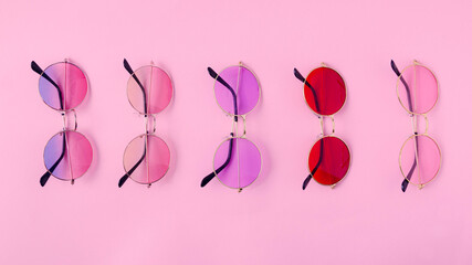 Obraz na płótnie Canvas Colorful tinted sun glasses neatly aligned on pastel pink background. Artistic design for wallpaper for summer season holidays. Flat lay