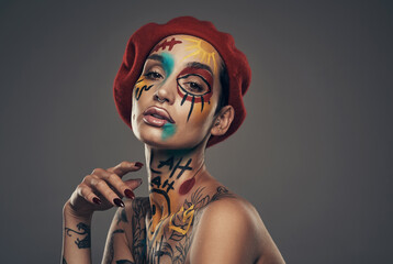Serving all kinds of attitude. Studio shot of a young woman posing with paint on her face on a grey...