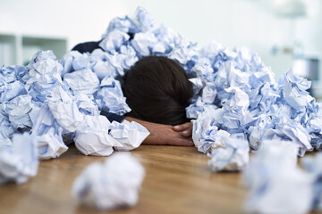 Overwhelmed in the workplace. Shot of an office worker passed out under a pile of crumpled up...