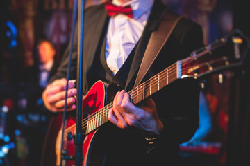 Concert view of an electric guitar player with vocalist and musical jazz band orchestra performing in the background, guitarist on the stage - obrazy, fototapety, plakaty
