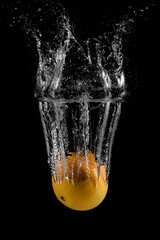 Fresh orange falls and flies into the water on a black background. Appetizing juicy fruit splashes in water. Food underwater. Bubbles and splashes of water. High speed food photography.