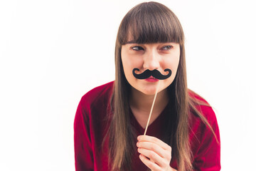 Pretty young woman holds fake moustache in front of her face and looks away movember concept white...