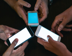 All for one and one for all. High angle shot of three unrecognizable people seated in a circle at a table while browsing on their cellphones.