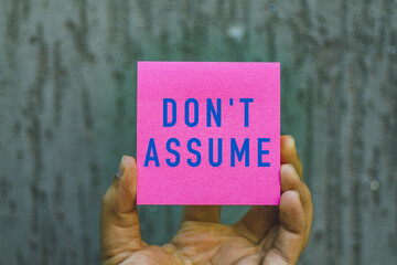 hand holding a note paper showing the words Don't Assume