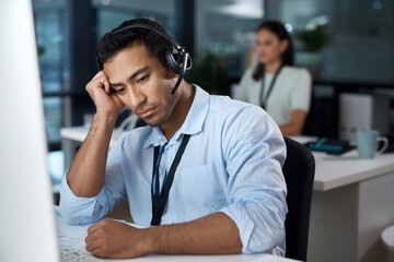 I need support too. Shot of a young man using a headset and looking depressed in a modern office.
