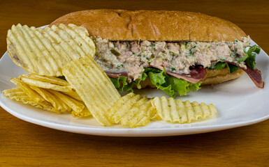 tuna salad sub  with bacon strips and a side of chips