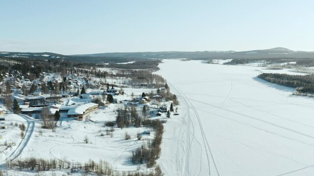 Aerial view of a winter village in Sweden. Snow-covered houses on the shores of a frozen lake in sunny weather with a beautiful landscape of nature.