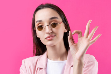 Portrait of beautiful young woman in pink jacket thinking isolated on red background. Shows an OK sign.