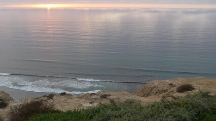 Dramatic cloudscape at sunset, reflection of sky and clouds. Torrey Pines scenic vista point, overlook viewpoint, ocean or sea water waves from above. Steep cliff, rock or bluff, California coast, USA