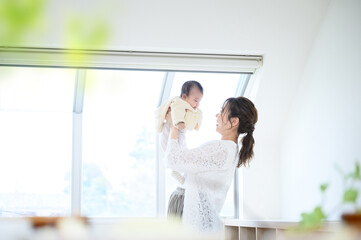 Fototapeta premium 明るい部屋で赤ちゃんを高い高いするお母さん