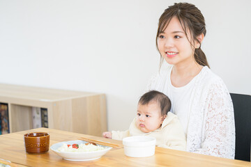 Obraz na płótnie Canvas 食卓で赤ちゃんと一緒にご飯を食べるママさん　左にコピースペースあり