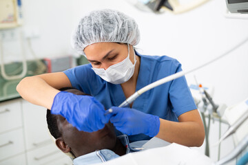 Dentist is treating male patient which is sitting in dental chair